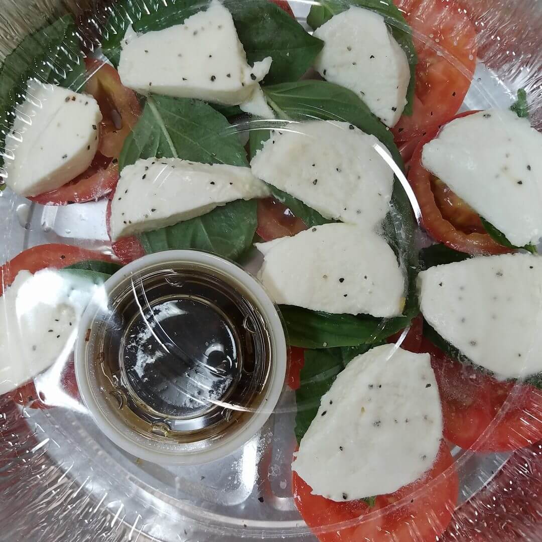 Sliced cheese on green leaves with a cup of dark sauce.