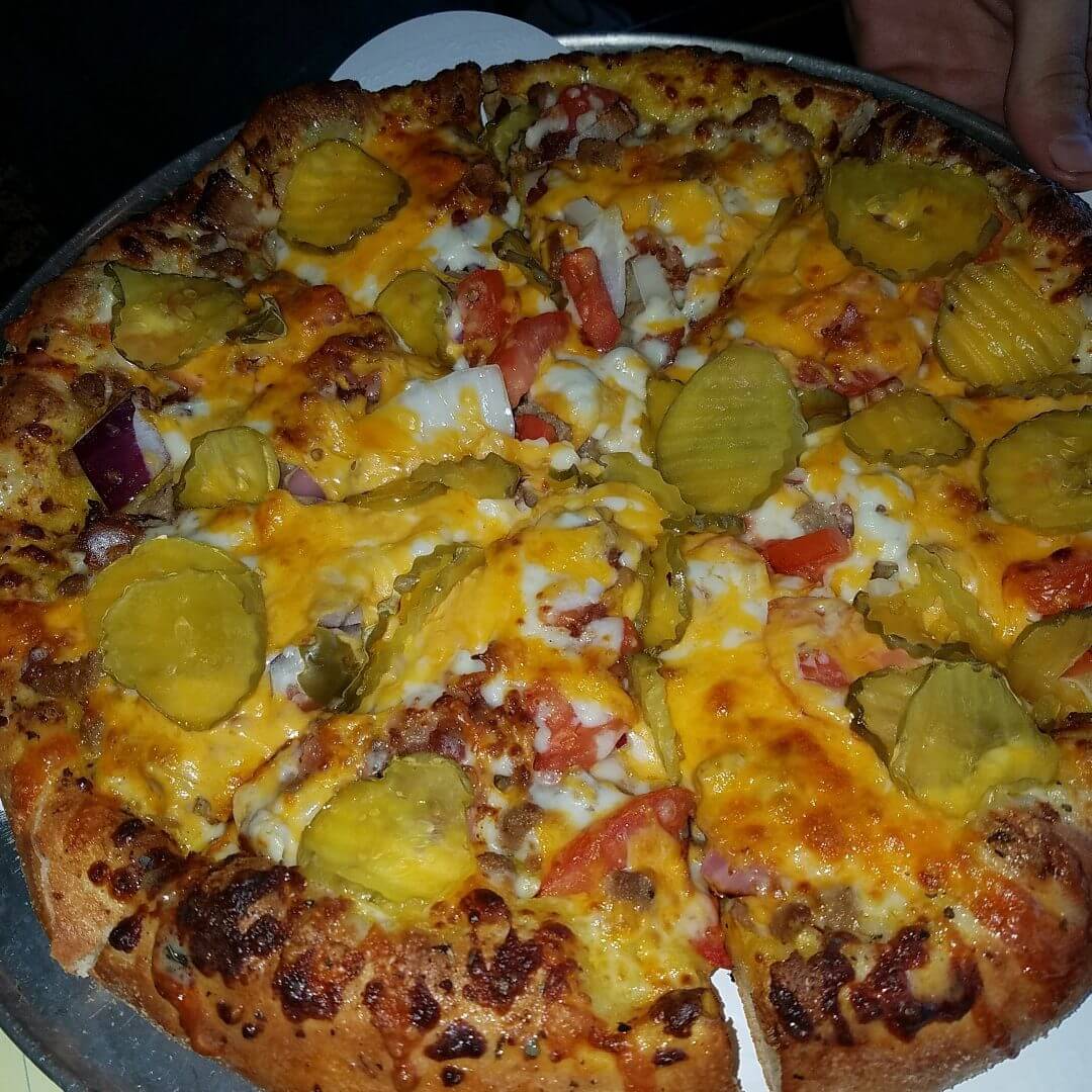 A cheesy pizza topped with pickles and diced tomatoes.
