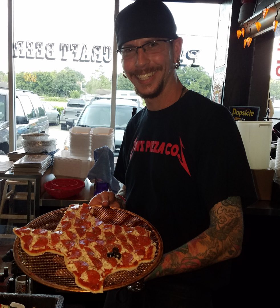 Man holding a large pepperoni pizza with a smile in a restaurant.