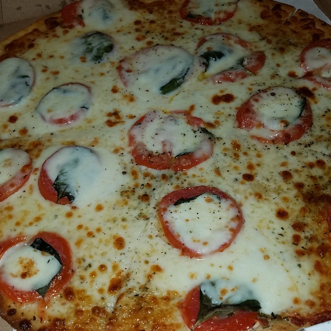 Close-up of a cheese pizza with sliced tomatoes and herbs.